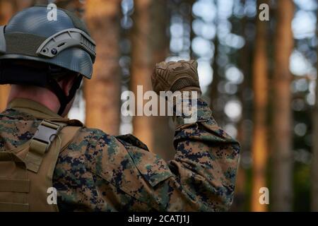 il soldato moderno della guerra sta mostrando i segnali tattici della mano per dare silenziosamente ordini e i generatori per l'ambiente della foresta della squadra Foto Stock