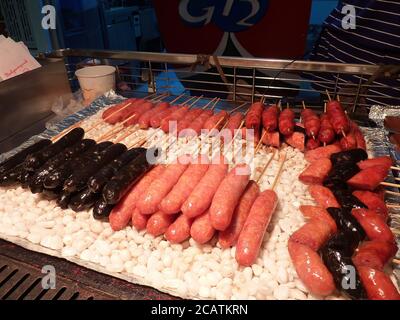 Primo piano di molti sapori diversi che grigliano salsiccia sulle pietre a Taipei, Taiwan Foto Stock