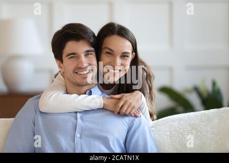 Felice bella giovane donna abbracciando un uomo sorridente seduto sul divano. Foto Stock