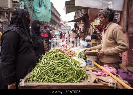 Agra / India - 22 febbraio 2020: L'uomo indiano allo stallo di strada che vende zenzero e fagioli alle donne musulmane che indossano abaya nero e niqab che copre la loro faccia tranne gli occhi Foto Stock