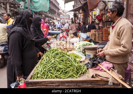 Agra / India - 22 febbraio 2020: L'uomo indiano allo stallo di strada che vende zenzero e fagioli alle donne musulmane che indossano abaya nero e niqab che copre la loro faccia tranne gli occhi Foto Stock