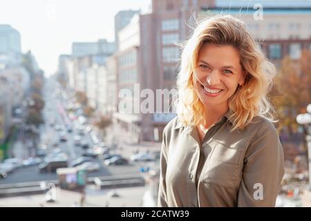 Splendida felice donna matura ridendo gioiosamente alla macchina fotografica, copia spazio. Splendida donna dai capelli biondi che gode di una calda giornata all'aperto in città Foto Stock