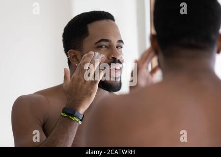 Primo piano positivo africano americano giovane uomo applicando crema viso Foto Stock