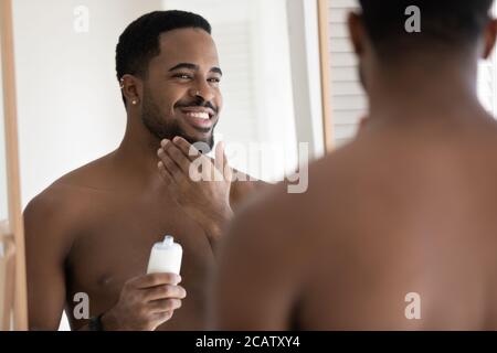 Specchio riflessione sorridente afroamericano che applica la lozione di aftershave Foto Stock