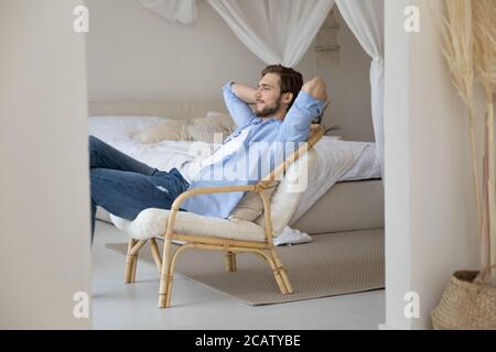 Soddisfatto calma giovane uomo rilassante stretching su sedia accogliente Foto Stock