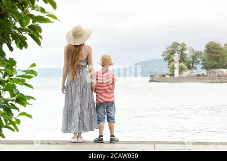Mamma e figlio in piedi sul molo, faro e montagne in lontananza. Vista posteriore Foto Stock