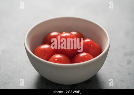 pomodori ciliegini maturi in ciotola bianca su una superficie di cemento Foto Stock