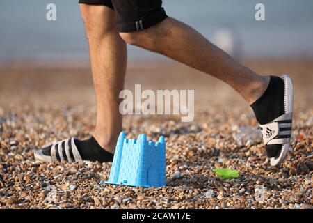 Brighton, Regno Unito. 09 agosto 2020. Un uomo cammina oltre un secchio di plastica di sabbia di castello scartato sulla spiaggia di Brighton, uno degli oggetti di maggio lasciato sulla spiaggia questa mattina dopo una giornata intensa ieri. Credit: James Boardman/Alamy Live News Foto Stock