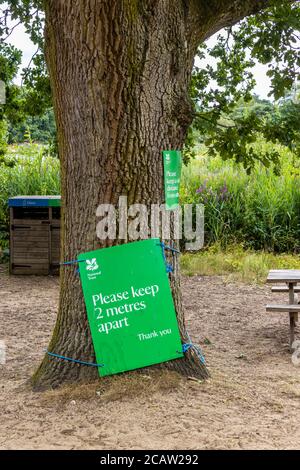 Un segno verde di allontanamento sociale del National Trust su un albero a Frensham Little Pond, un luogo di bellezza popolare in Surrey, Inghilterra sud-orientale Foto Stock