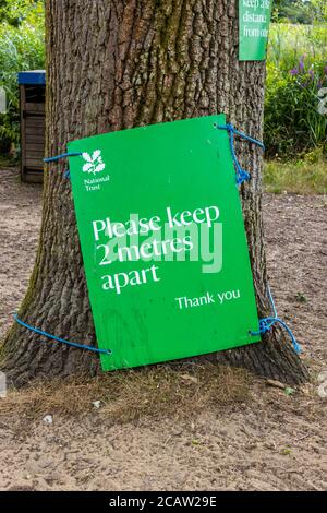 Un segno verde di allontanamento sociale del National Trust su un albero a Frensham Little Pond, un luogo di bellezza popolare in Surrey, Inghilterra sud-orientale Foto Stock