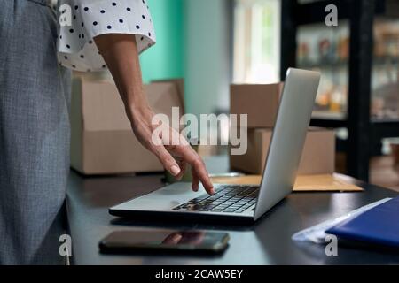 Prendere gli ordini online. Un'immagine ritagliata di una donna, una donna che usa un computer portatile mentre si trova in negozio o in negozio. Mettere a fuoco la mano femminile. Piccola impresa, vendita al dettaglio Foto Stock