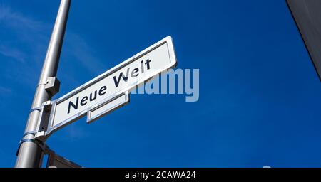'Neue Welt' (in tedesco: 'New World') insolito segno di strada nome strada contro un cielo blu nel quartiere Friedrichshain di Berlino, Germania. Foto Stock
