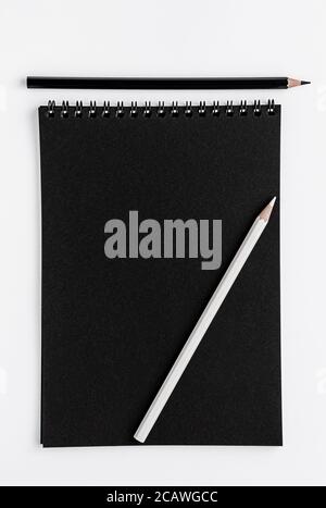 Mockup e matite di sketchbook neri su sfondo bianco. Vista dall'alto, spazio di copia Foto Stock