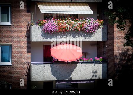 casa di città vecchia con balconi, gerani con fiori rossi su uno, ombrellone sull'altro balcone Foto Stock