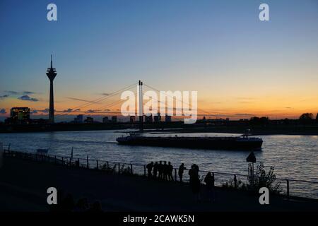 Vista panoramica con un romantico tramonto sul fiume Reno a Düsseldorf, con i due punti di riferimento della torre del Reno e Rheinkniebrücke e una nave che passa. Foto Stock
