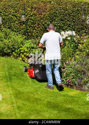 Uomo che taglia un prato con un tosaerba rotante in Un cottage inglese giardino Inghilterra UK Foto Stock