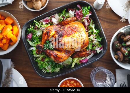 Decorato tavolo festivo con pollo arrosto intero, insalata, zucca, funghi, fagioli e noce. Il concetto di cena di famiglia o di celebrazione del Ringraziamento Foto Stock