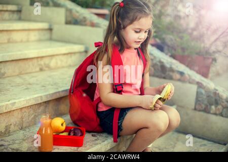 Allievo che ha un pranzo seduto su una scala all'aperto. Ritorno a scuola. Foto Stock