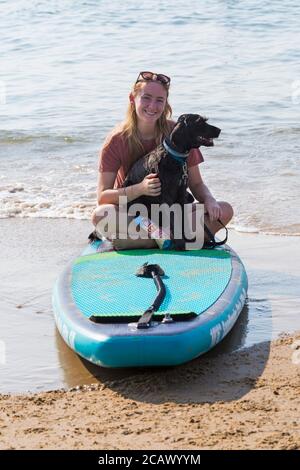 Giovane donna seduta su paddleboard, paddle board, con cane cockapoo seduto in grembo a Poole, Dorset, Regno Unito, nella calda giornata di sole in agosto Foto Stock