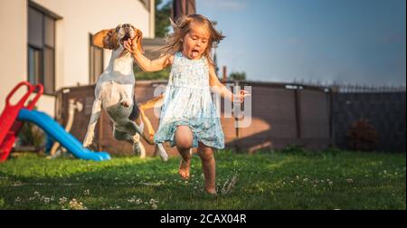 Bambina che corre con cane beagle in giardino il giorno d'estate. Animale domestico con concetto di bambino. Foto Stock