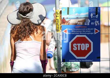 Timmendorfer Strand, Germania. 09 agosto 2020. I bagnanti che passano per un accesso chiuso alla spiaggia del Mar Baltico passeranno un cartello con un segnale di stop e l'iscrizione 'attenzione - questa sezione di spiaggia è occupata - si prega di utilizzare una delle sezioni di spiaggia successive! Credit: Bodo Marks/dpa/Alamy Live News Foto Stock