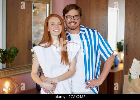 ritratto di adorabile coppia caucasica al chiuso, a casa. giovane ragazzo bearded e ragazza rossa abbraccio e guardare la macchina fotografica, sorridere Foto Stock