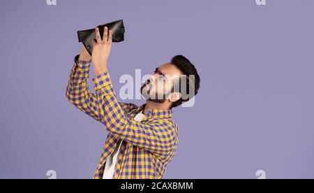 Concetto di crisi economica. Un ragazzo indiano sconvolto con un portafoglio vuoto su sfondo viola Foto Stock
