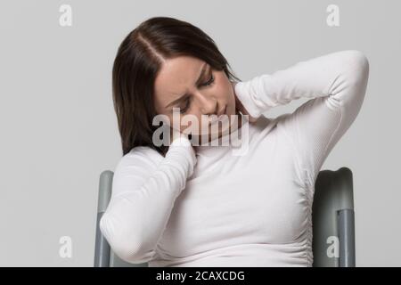 Ritratto closeup di una donna malsana in cima bianca con dolore al collo e alla schiena. Artrite cervicale, osteocondrosi, malattie muscoloscheletriche Foto Stock