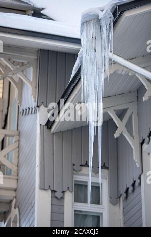 Tetto di un edificio in legno coperto di acini affilati. Icicolo acuto appeso ad un tubo di scarico. Uno scarso isolamento termico del tetto porta alla formazione Foto Stock