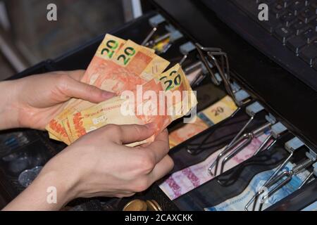 Il venditore passa al registratore di cassa con le banconote in denaro brasiliane e. monete all'interno del registratore di cassa elettronico Foto Stock