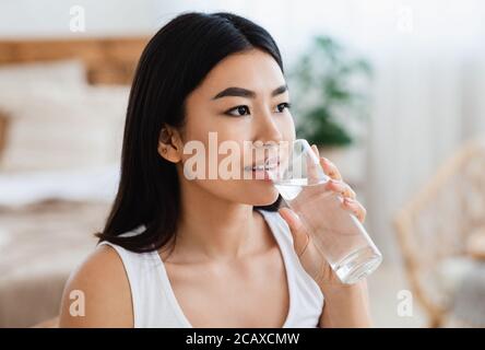 Giovane ragazza asiatica che beve acqua in camera da letto a casa Foto Stock