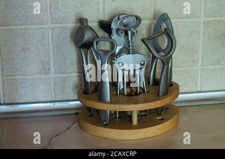 Utensili da cucina in metallo in un supporto di legno. Cavatappi, apribottiglie, coltello speciale, apribera, nutcracker e pressa all'aglio sul tavolo da cucina. Vita st Foto Stock
