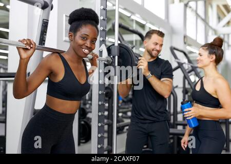 l'addestratore caucasico sta insegnando gli esercizi con i pesi alle donne attraenti differenti, dumbbell, corso di sollevamento del barbell per aumentare i muscoli del corpo per essere stro Foto Stock