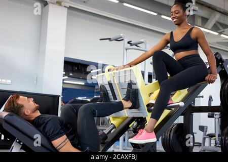 il formatore traccia la correttezza dell'esercizio in palestra, insegna alle persone a svolgere esercizi con pesi Foto Stock