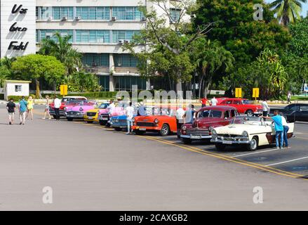 Gamma di auto classiche e colorate a Revolution Square. Cubano guida in attesa di turisti a guidare i veicoli d'epoca a l'Avana, Cuba. Foto Stock