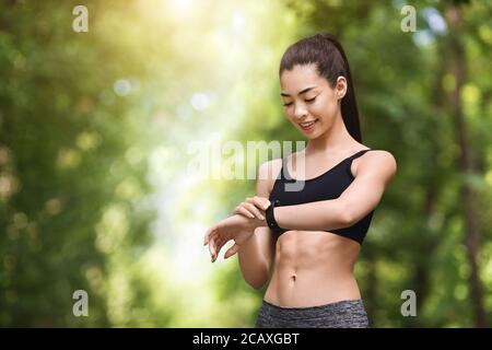 Ragazza asiatica che guarda la fascia cardio sullo smartwatch dopo jogging all'aperto Foto Stock