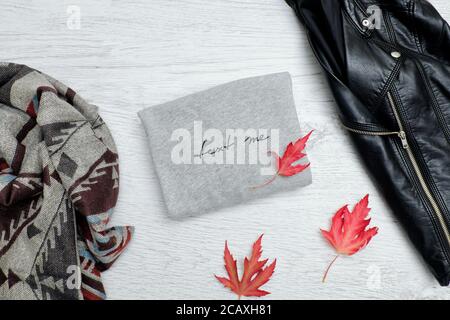 Maglione grigio con iscrizione, giacca nera, sciarpa e foglie d'autunno. Concetto alla moda Foto Stock