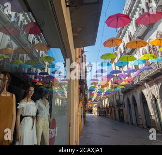 Glesias, Italia: Ombrelli colorati appesi su una strada nella vecchia città di Iglesias in una giornata di sole Foto Stock