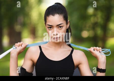 Motivazione dello sport. Ragazza asiatica seria che posa con la corda di salto all'aperto Foto Stock