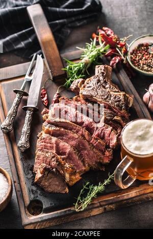 Fette di carne di manzo succosa bistecca coltello spezie sale pepe erbe e birra alla spina Foto Stock
