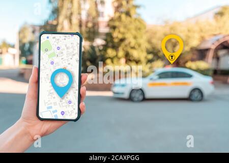 Una donna ha un cellulare con un'app mappa online, primo piano mano. Sullo sfondo si trova una strada cittadina con taxi. Il concetto di navigazione online An Foto Stock