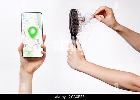 Le mani delle donne puliscono il pettine dai capelli caduti e tiene uno smartphone con un'app online Maps. Sfondo bianco. Il concetto di ricerca on-line della bellezza s Foto Stock