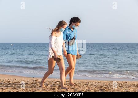 Punta Umbria, Huelva, Spagna - 7 agosto 2020: Due giovani Donne che camminano sulla spiaggia indossando maschere protettive o mediche. Nuova normalità in Spagna con Foto Stock