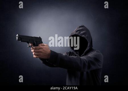 Uomo incappucciato con una pistola nel buio Foto Stock