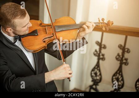 un giovane professionista di talento suona con grazia il violino, un bel musicista in una tuta elegante e formale esegue musica classica Foto Stock