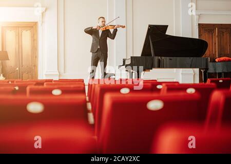 il giovane caucasico di talento pratica il violino su un palcoscenico, il musicista professionista che si esibirà in musica classica per il pubblico Foto Stock