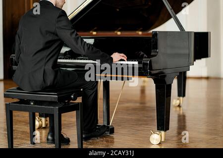 un maschio non riconoscibile in tuta che suona il piano su un palcoscenico. bel ragazzo suona il piano, pratica prima della performance Foto Stock