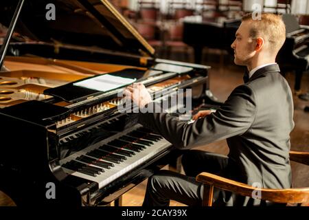 il musicista professionista dell'uomo caucasico suona con grazia il pianoforte su un palcoscenico, pianista di talento in abito elegante formale esegue musica Foto Stock