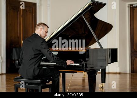 il giovane e bel caucasico in elegante abito formale suona con grazia il pianoforte, mentre il pianista professionista esegue musica classica Foto Stock