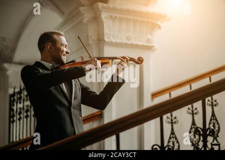 il violinista maschile caucasico professionista di talento suona nella sala, pratica prima dello spettacolo. concetto di musica classica. l'uomo in tuta esegue musica utilizzando Foto Stock